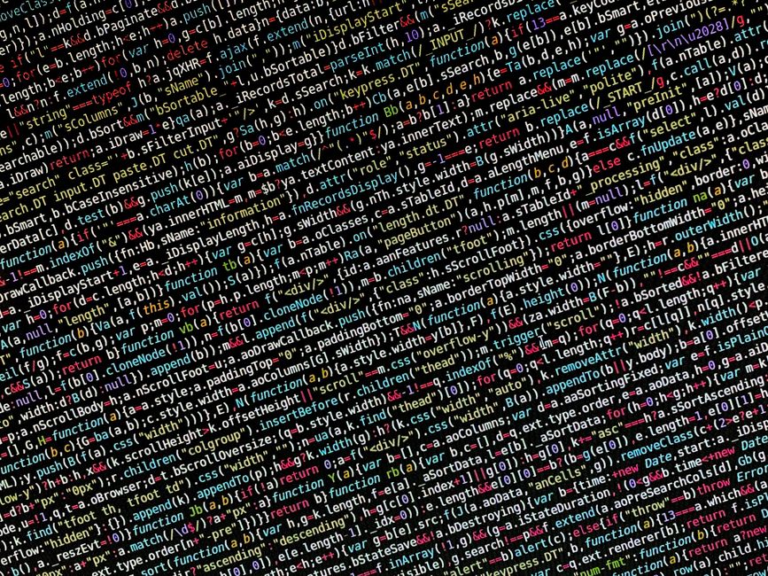 Close-up of a person's hands operating a laptop on a dark surface, displaying lines of code on the screen related to software development or data management. The person is using a MacBook with a black